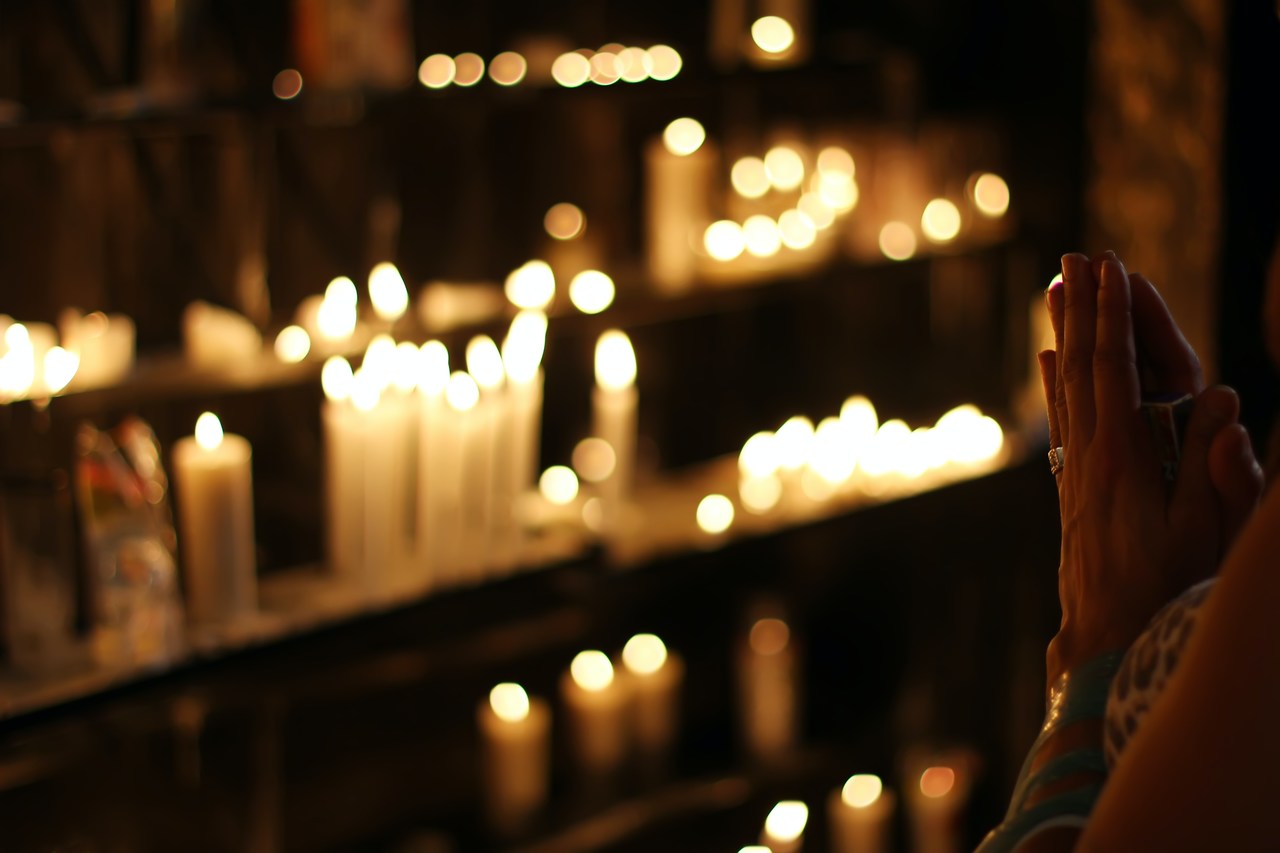 ciências da religião - pessoa com as mãos unidas em prece em frente a diversas velas acesas