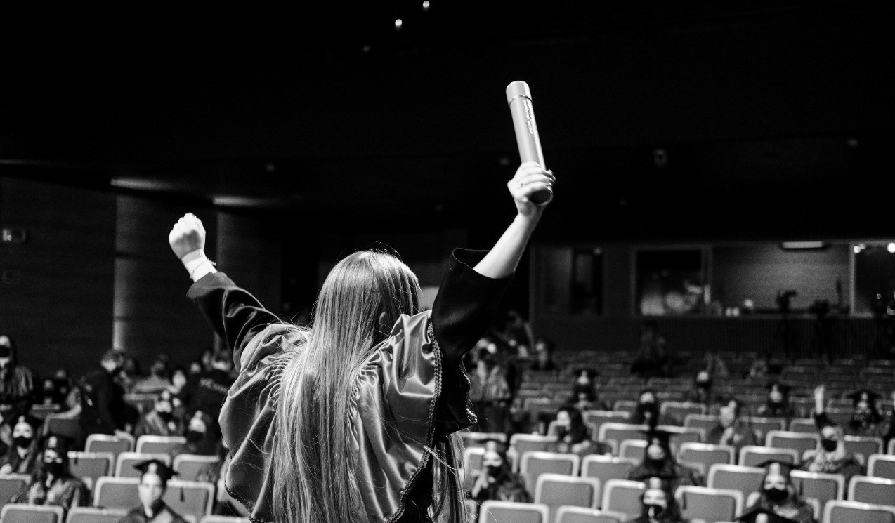 menina segurando diploma com as mãos erguidas para o alto, em comemoração.