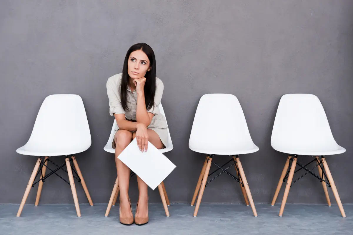 Fui demitido, como explicar na entrevista de emprego - jovem sentada em cadeira branca e segurando papel com expressão de espera